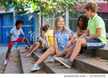 Children talking together while sitting on stairs outdoors Children talking together while sitting on stairs outdoors 125882850