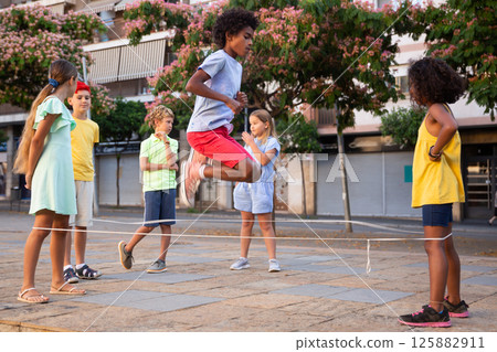 Happy tweenagers playing chinese jump rope in city square 125882911