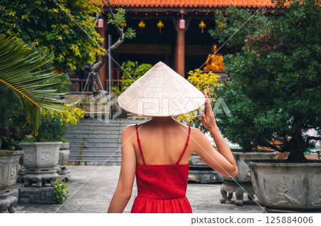back of a female tourist traveler in a Vietnamese hat at Long Son Pagoda in Nha Trang in Vietnam. Travel and tourism in Asia 125884006