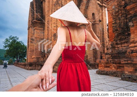 Back of a female tourist traveler in Vietnamese hat Non La at Po Nagar Cham Towers in Nha Trang in Vietnam. The concept of follow me, traveling in Asia Back of a female tourist traveler in Vietnamese hat Non La at Po Nagar Cham Towers in Nha Trang in Vietnam. The concept of follow me, traveling in Asia 125884010