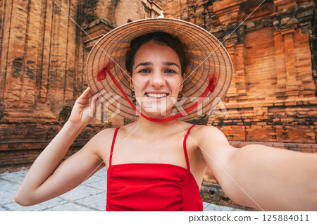 happy young female tourist traveler in a Vietnamese hat takes a selfie at Cham Towers of Po Nagar in Nha Trang in Vietnam in Asia happy young female tourist traveler in a Vietnamese hat takes a selfie at Cham Towers of Po Nagar in Nha Trang in Vietnam in Asia 125884011