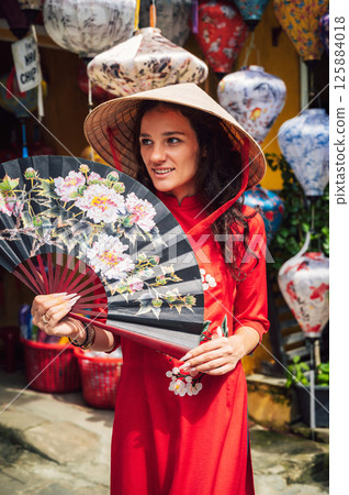 happy beautiful tourist woman in Vietnamese cone hat Non La with fan in Hoi An in Vietnam in Asia 125884018