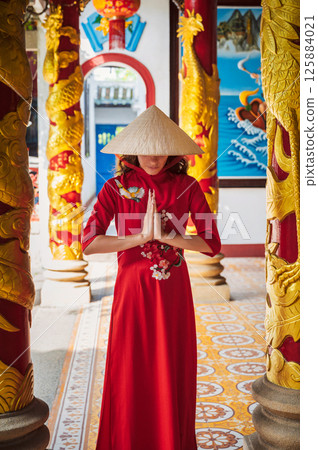Asian young woman in a traditional Vietnamese hat and costume prays at a temple on Buddhist pagoda in Vietnam in Asia Asian young woman in a traditional Vietnamese hat and costume prays at a temple on Buddhist pagoda in Vietnam in Asia 125884021
