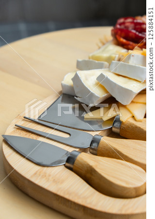 Cheese and meat charcuterie board. Gift present idea, dinner lunch plate. Minimal effort visually pleasing snacks. Simple meal preparation with special cheese knives Cheese and meat charcuterie board. Gift present idea, dinner lunch plate. Minimal effort visually pleasing snacks. Simple meal preparation with special cheese knives 125884151