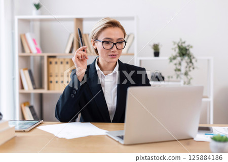 Businesswoman working on laptop at desk in office, analyzing report. Focused, professional, and diligent, portraying concepts of business analysis, professionalism, and office work 125884186