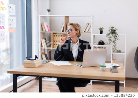 Confident businesswoman in her thirties working at desk in bright modern office setting Confident businesswoman in her thirties working at desk in bright modern office setting 125884220