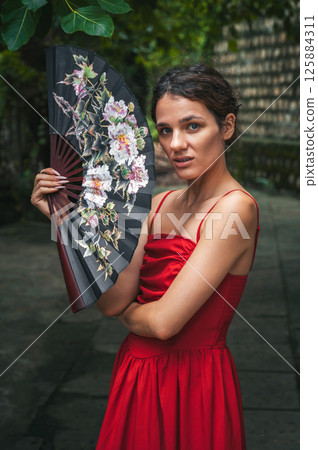 beautiful young woman in a red dress with a fan in garden. Tourism and travel in Asia 125884311