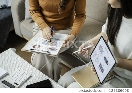 Two professionals reviewing financial charts on a tablet and clipboard during a business meeting in a modern office environment. Two professionals reviewing financial charts on a tablet and clipboard during a business meeting in a modern office environment. 125886008