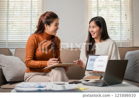 Two women discussing business strategies using digital devices in a bright, modern office environment. 125886010