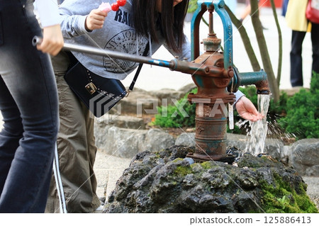 A girl washes her hands with water from a hand pump 125886413