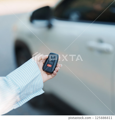 Hand holding car remote control, smart key to lock or unlock doors of white car. Safety, travel and transportation concept 125886811