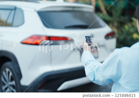 Hand holding car remote control, smart key to lock or unlock back door of white car. Safety, travel and transportation concept Hand holding car remote control, smart key to lock or unlock back door of white car. Safety, travel and transportation concept 125886815