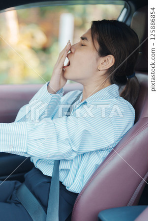 woman feeling sleepy and yawn during drive car long time. Asian girl tired and fatigue having headache after driving car in traffic jam. Sleep, stretching and safety concept 125886854
