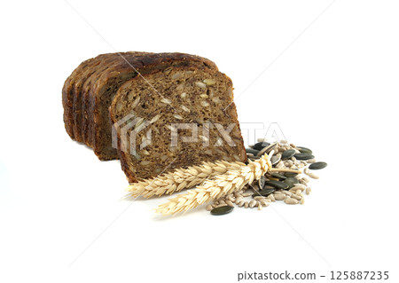 A sliced loaf of dark rye bread with mixed seeds and wheat stalks arranged on a white background. A sliced loaf of dark rye bread with mixed seeds and wheat stalks arranged on a white background. 125887235