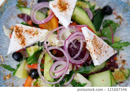 greek salad in plate isolated Salad cheese onions Fresh healthy vegetable Mediterranean salad of feta cheese, tomato, olives, green pepper and green basil leaves, top view 125887346