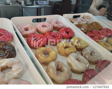 Donuts in a tray with colored glaze and sprinkled with chocolate nuts. National Sweetness 125887682