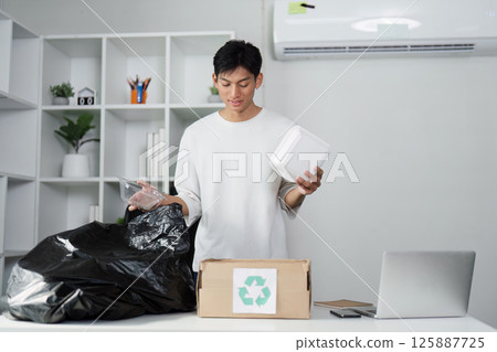 Young man examining recyclable containers in eco-friendly workspace, promoting recycling and sustainable living. 125887725