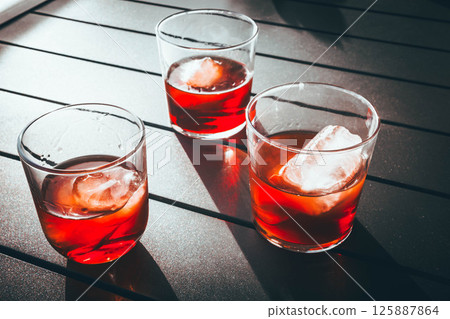 Three glasses of red vermouth with ice on a terrace table under sunlight Three glasses of red vermouth with ice on a terrace table under sunlight 125887864
