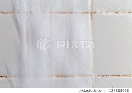 I'm using foam to clean the mold in the grooves of the bathroom tiles. 125888088