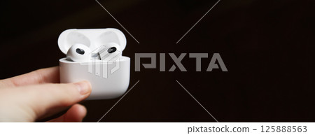 Black headphones or airpods in hand against a black background. Copy space for your text. Modern audio technology. Banner for design Black headphones or airpods in hand against a black background. Copy space for your text. Modern audio technology. Banner for design 125888563