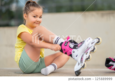 Little girl wearing roller-skates preparing for outdoor skating Little girl wearing roller-skates preparing for outdoor skating 125889999