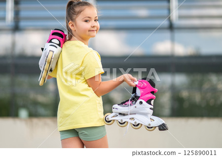 Energetic female child holding roller-skates playing outside 125890011