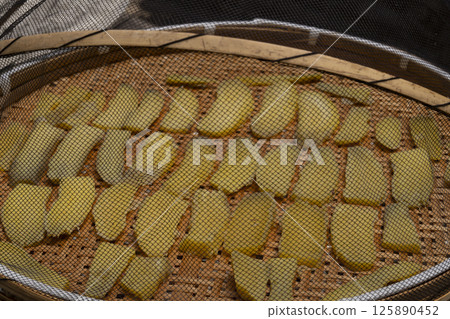 The process of making dried sweet potatoes. Sweet potatoes are lined up on a drying rack and dried in the sun. 125890452