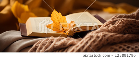 Autumn leaves. An open book near a knitted blanket with a fallen leaf close up. 125891796