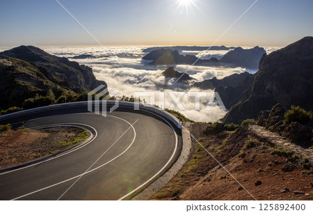 Epic Sunset View in High Mountain Landscape with Asphalt Road . Pico do Arieiro , Madeira Island . Clouds in the Valley . Epic Sunset View in High Mountain Landscape with Asphalt Road . Pico do Arieiro , Madeira Island . Clouds in the Valley . 125892400