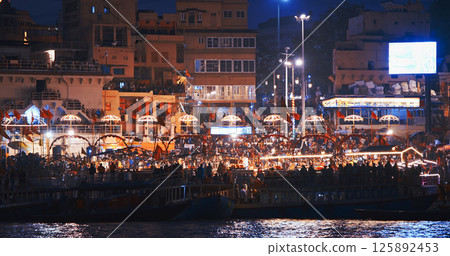 Varanasi, Uttar Pradesh, India. Many people visiting Ganga Maha Aarti ceremony on Dashashwamedh Ghat. night time illumination lights. Cinematic Camera movement moving along riverbank embankment. View 125892453