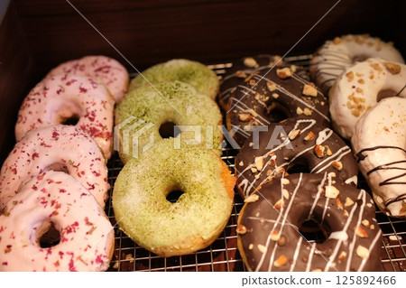 Color donuts in box on wood table from top view. variety of colorful donuts arranged in a box, featuring a mix of glazed, chocolate-coated, and sprinkled toppings. The assortment includes donuts 125892466