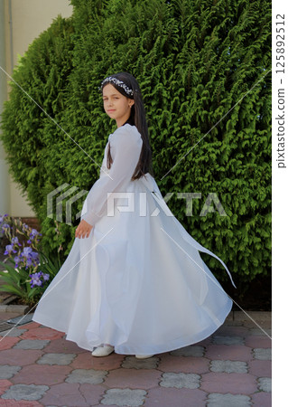The child stands in a light dress. The ivory outfit creates an image of spiritual purity. 125892512