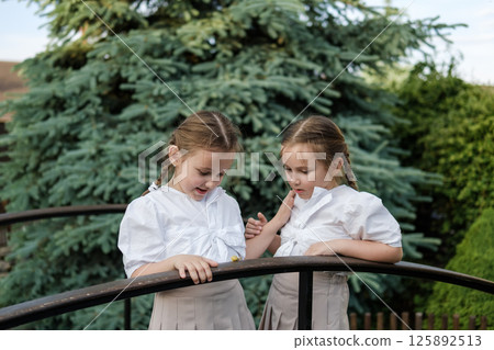Little girls with identical hairstyles observe the snail on the railing. The twins appear curious and gentle. 125892513
