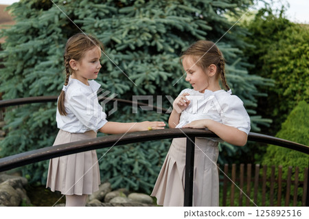 Little girls in white clothing stand beside the wooden railing. A snail crawls along the railing, fully capturing the twins' attention 125892516
