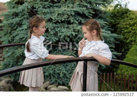 Little girls in white clothing stand beside the wooden railing. A snail crawls along the railing, fully capturing the twins' attention 125892517