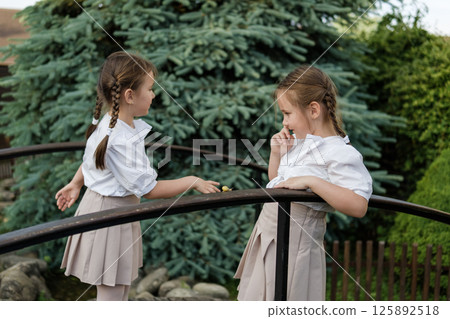 Little girls in white clothing stand beside the wooden railing. A snail crawls along the railing, fully capturing the twins' attention 125892518