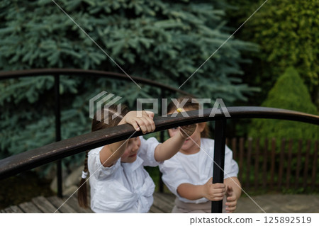 Twins in light clothing carefully examine the snail. The girls' braids are neatly tied and fall over their shoulders. 125892519