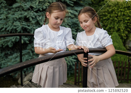 Twin girls stand close and lean over the railing. The snail moves gently, capturing both children's attention. 125892520