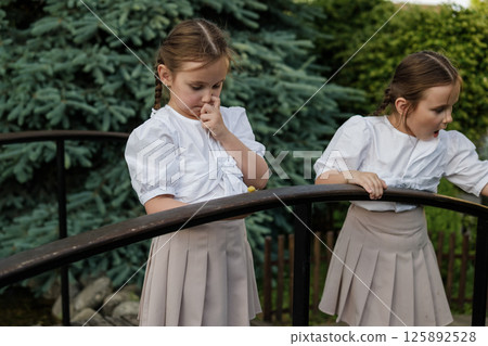The twins observe the snail moving along the railing. Attentive girls in identical outfits create a sense of harmony. 125892528
