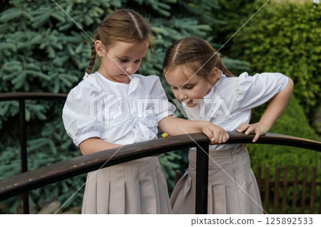 The twins carefully examine the snail crawling along the wooden surface. The girls with two braids look sweet and harmonious 125892533