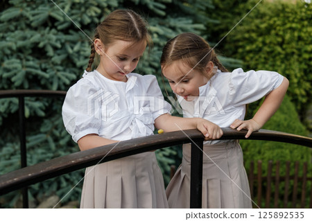 The twins carefully examine the snail crawling along the wooden surface. The girls with two braids look sweet and harmonious. The twins carefully examine the snail crawling along the wooden surface. The girls with two braids look sweet and harmonious. 125892535