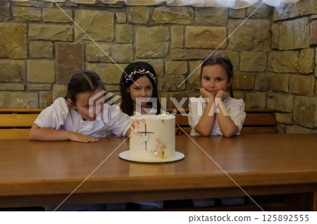 The twin girls and their older sister settled at the wooden table in a festive setting. The decorated cake became the focal point for all the girls. 125892555