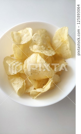 Crispy golden potato chips piled in a white bowl with a light seasoning, perfect snack for gatherings or casual moments of indulgence and enjoyment Crispy golden potato chips piled in a white bowl with a light seasoning, perfect snack for gatherings or casual moments of indulgence and enjoyment 125893064