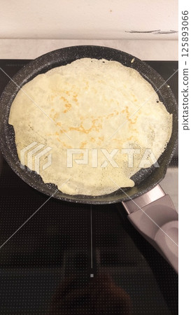Golden-brown crepe cooking in a non-stick skillet on a modern stovetop with a smooth surface highlighting culinary artistry and home cooking experience 125893066