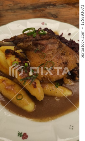 Golden-brown roasted duck leg served with creamy potato dumplings and rich gravy, garnished with fresh green onions, inviting comfort food experience Golden-brown roasted duck leg served with creamy potato dumplings and rich gravy, garnished with fresh green onions, inviting comfort food experience 125893073