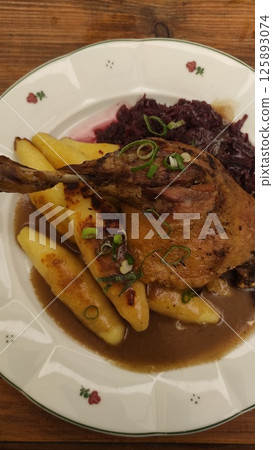 Succulent roasted chicken leg served with golden crispy potatoes and vibrant red cabbage, garnished with fresh green onions for a delightful culinary experience 125893074