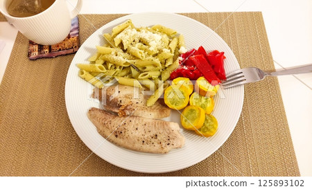 Delicious meal featuring grilled fish, pesto pasta, and roasted vegetables 125893102