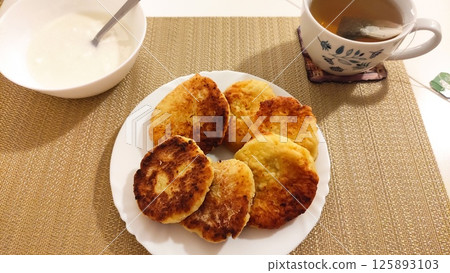 Syrniki, cottage cheese pancakes with sour cream and tea on tablecloth for breakfast 125893103