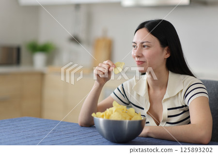 Happy asian woman eating potato chips in the kitchen 125893202