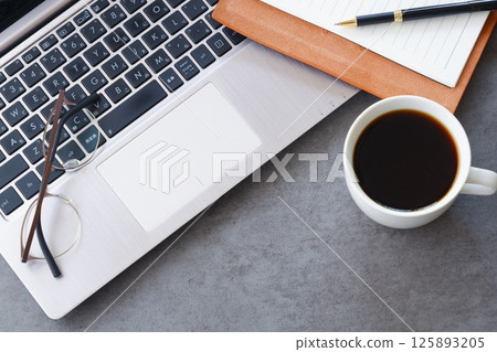 An image of someone working at a desk with a laptop and a personal organizer while drinking freshly brewed delicious coffee 125893205